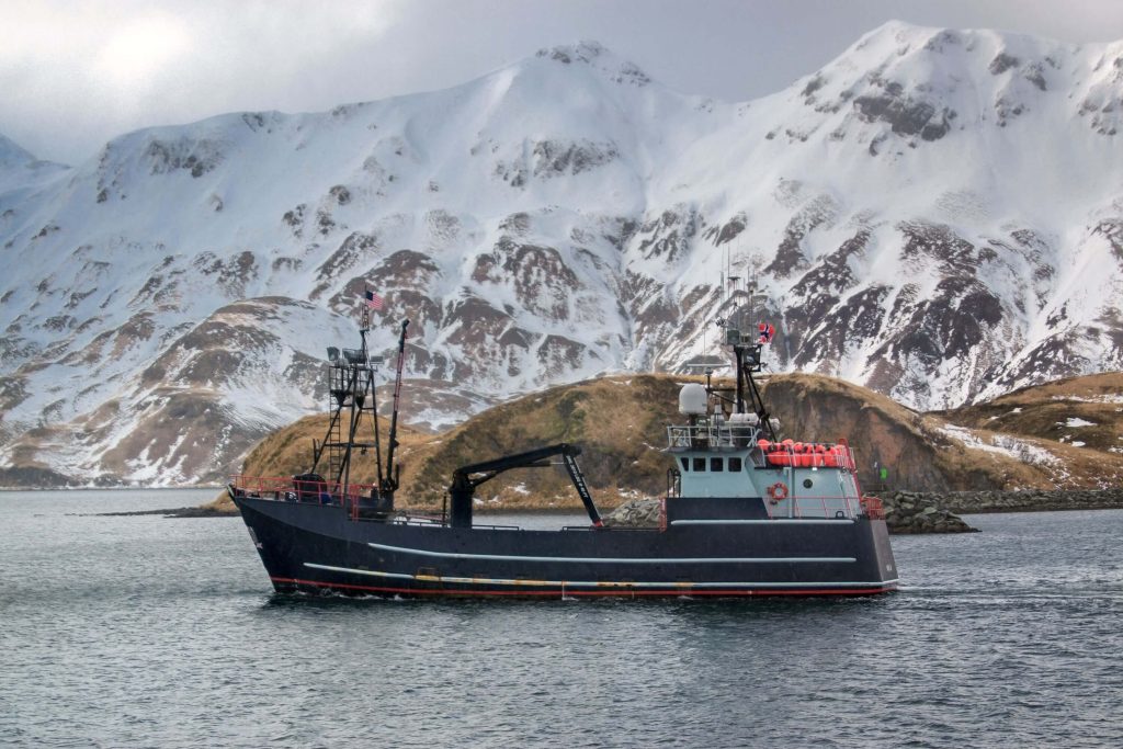 Barco de cangrejo comercial que viaja con fondo de montaña nevada en Alaska